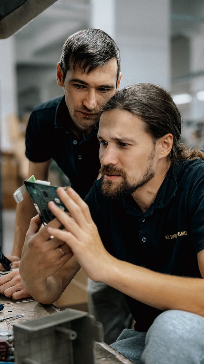 services-img Two engineers closely inspecting a green circuit board for electronic components.